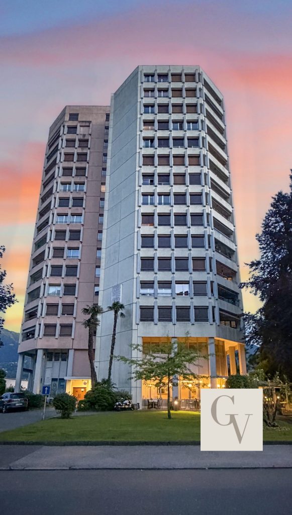 Airbnb Ticino, Fotografie del tramonto a Palazzo Panorama Locarno, con cieli serali dai colori vivaci, appartamenti illuminati da una luce calda, spazi commerciali, ristorante, immobili professionali e fotografie per Airbnb in Ticino, Svizzera. Palazzo Panorama Locarno sunset photography featuring colorful evening skies, warmly lit apartment, commercial spaces, restaurant, professional real estate and Airbnb photography in Ticino, Switzerland.